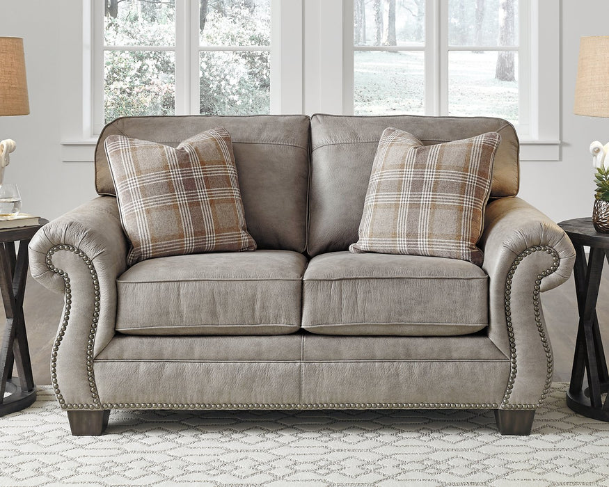 Olsberg loveseat in a cozy living room, featuring steel gray upholstery, plaid accent pillows, and nailhead trim.