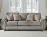 Olsberg sofa in a modern living room, featuring steel gray upholstery, nailhead trim, and plaid accent pillows.