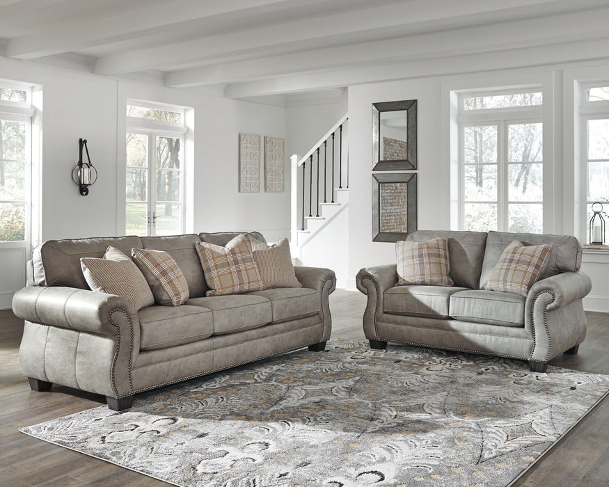 Olsberg sofa and loveseat in a stylish living room, featuring steel gray upholstery, plaid pillows, and nailhead trim.