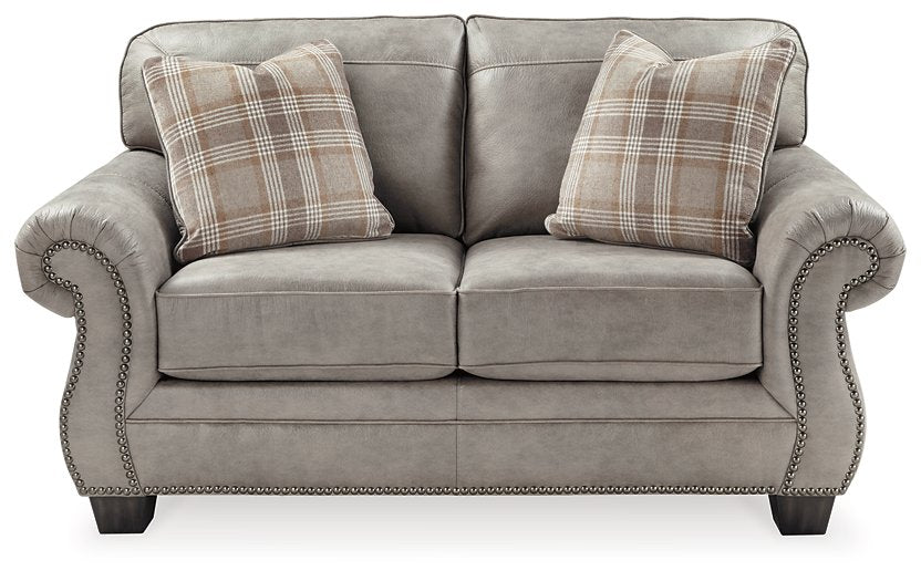 Front view of the Olsberg loveseat with steel gray upholstery, plaid accent pillows, and nailhead trim for elegant style.