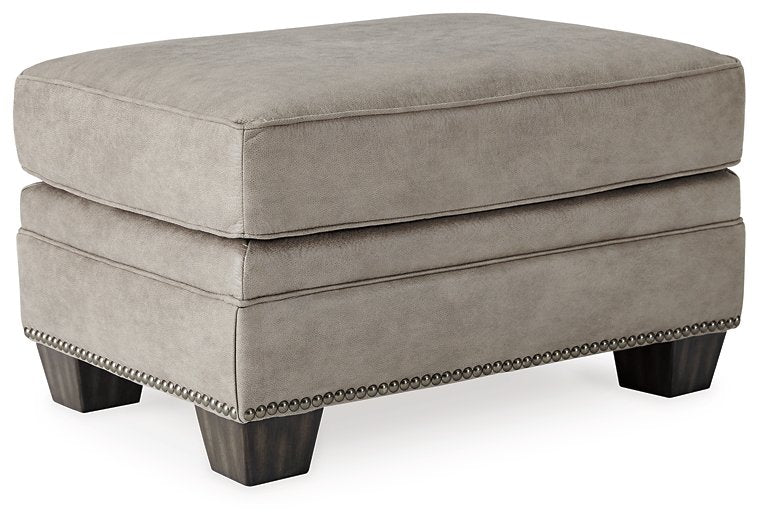 Front view of the Olsberg ottoman with steel gray upholstery, nailhead trim, and faux wood legs for added style.